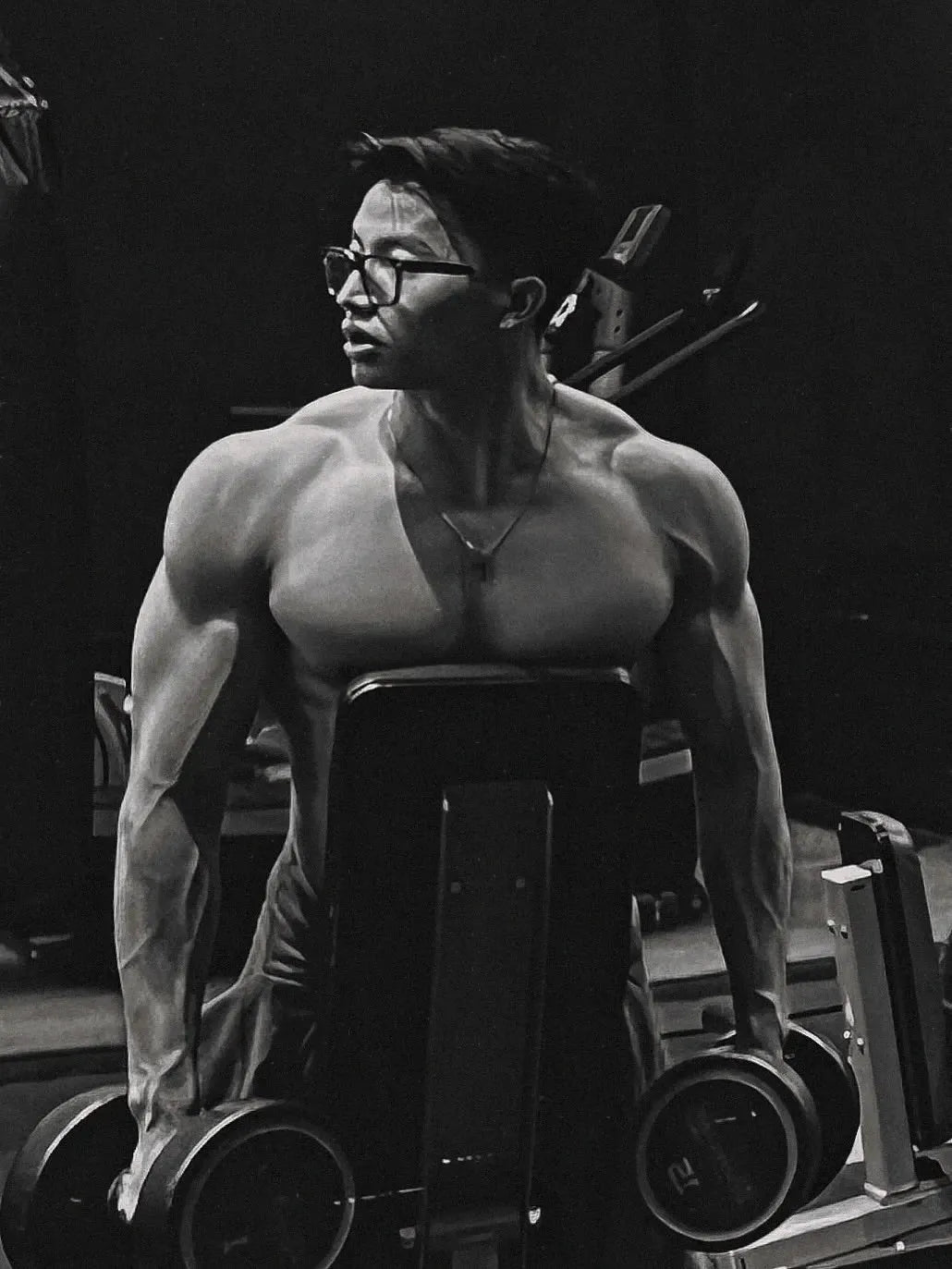 Muscular man with glasses lifting dumbbells in gym, demonstrating strength and fitness